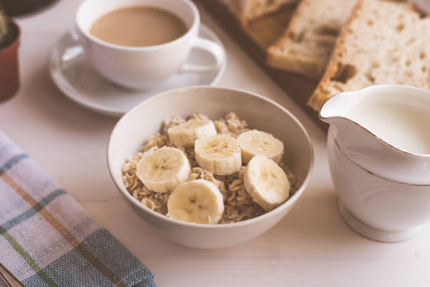farina d'avena con banana e caffè con latte per colazione - primo piano, su uno sfondo rustico leggero - steel cut oats foto e immagini stock