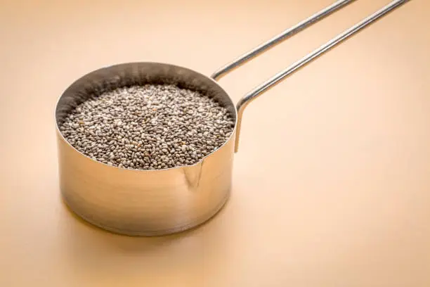 chia seeds in metal measuring scoop against beige background