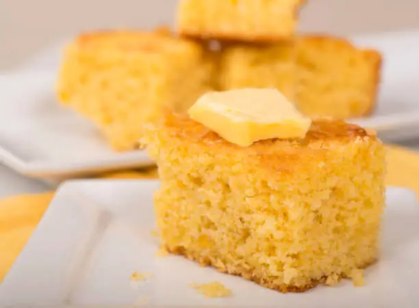 Piece of freshly baked cornbread with creamy butter on top.