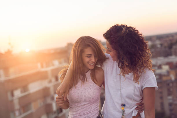 Lesbian couple Lesbian couple standing and hugging on a building rooftop at sunset, affectionate and happy, with cityscape in the background lesbians stock pictures, royalty-free photos & images