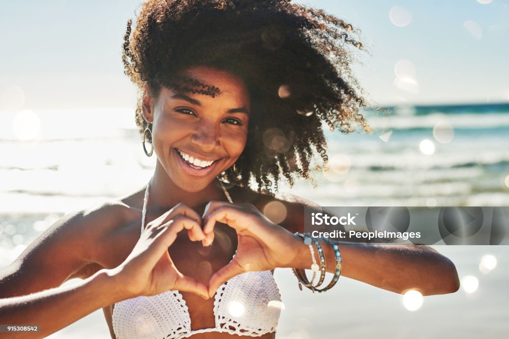 My heart belongs to summer Portrait of a beautiful young woman making a heart shaped gesture with her hands at the beach Beach Stock Photo