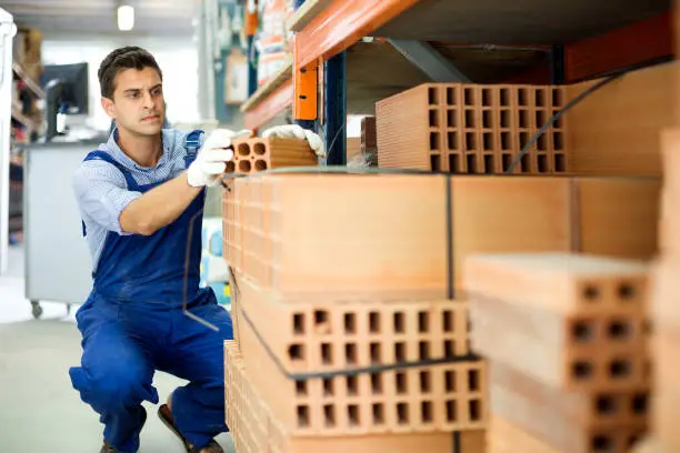 Serios shop assistant man is checking quality of bricks in store.