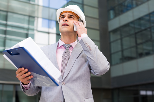 Business man talking on mobile phone outdoors with documents in hand