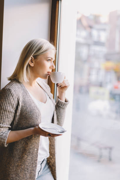 istock Young woman drinking coffee, looking through the window. 915314674