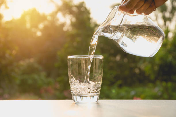 Person pouring water from pitcher to glass on nature background stock photo
