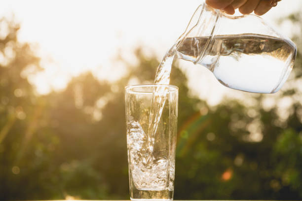 Person pouring water from pitcher to glass on nature background stock photo