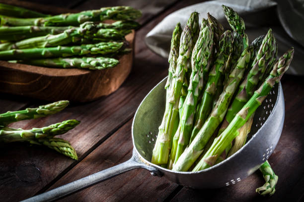Fresh organic asparagus in an old metal colander shot on rustic wooden table. This vegetable is considered a healthy salad ingredient. Predominant colors are green and brown. Low key DSRL studio photo taken with Canon EOS 5D Mk II and Canon EF 100mm f/2.8L Macro IS USM