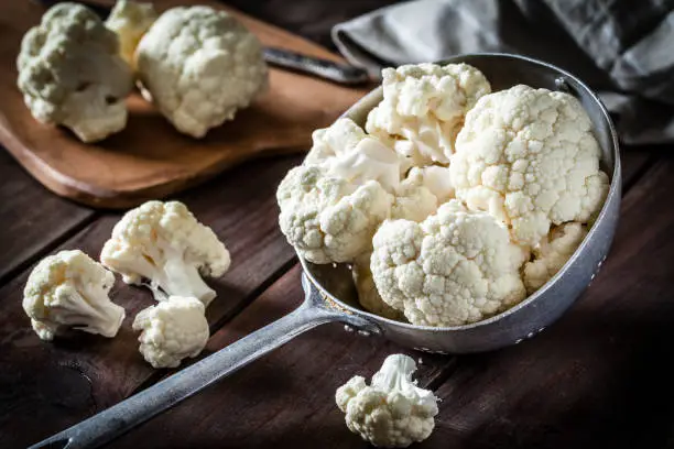 Fresh organic cauliflower in an old metal colander shot on rustic wooden table. This vegetable is considered a healthy salad ingredient. Predominant colors are white and brown. Low key DSRL studio photo taken with Canon EOS 5D Mk II and Canon EF 100mm f/2.8L Macro IS USM