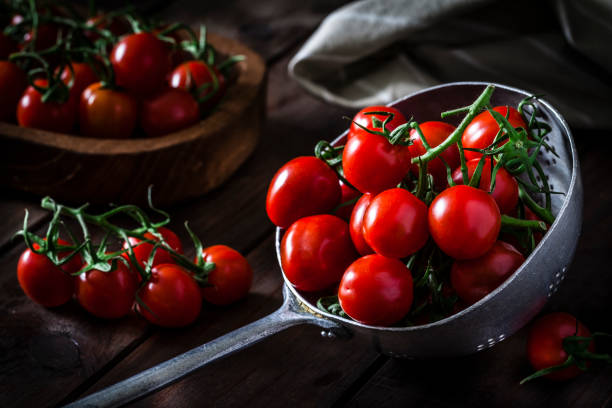 Fresh organic cherry tomatoes in an old metal colander shot on rustic wooden table. Predominant colors are red and brown. Low key DSRL studio photo taken with Canon EOS 5D Mk II and Canon EF 100mm f/2.8L Macro IS USM