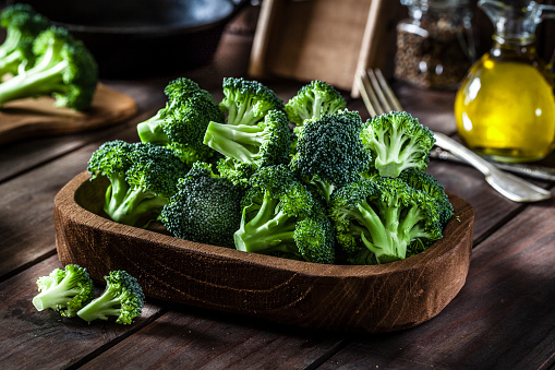 Fresh organic broccoli in a wooden tray shot on rustic wooden kitchen table. This vegetable is considered a healthy salad ingredient. Predominant colors are green and brown. Low key DSRL studio photo taken with Canon EOS 5D Mk II and Canon EF 100mm f/2.8L Macro IS USM