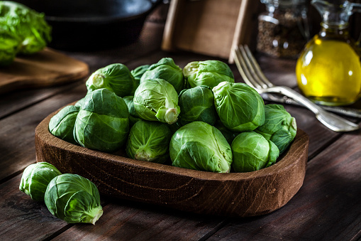 Fresh organic Brussels sprouts in a wooden tray shot on rustic wooden kitchen table. This vegetable is considered a healthy salad ingredient. Predominant colors are green and brown. Low key DSRL studio photo taken with Canon EOS 5D Mk II and Canon EF 100mm f/2.8L Macro IS USM