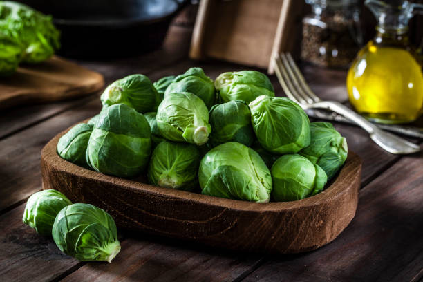 Fresh organic Brussels sprouts shot on rustic wooden table Fresh organic Brussels sprouts in a wooden tray shot on rustic wooden kitchen table. This vegetable is considered a healthy salad ingredient. Predominant colors are green and brown. Low key DSRL studio photo taken with Canon EOS 5D Mk II and Canon EF 100mm f/2.8L Macro IS USM brussels sprout stock pictures, royalty-free photos & images