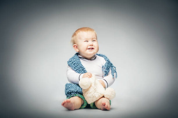 Pretty blond boy in cute pastel clothes, holding a beanie, looking up and laughing.