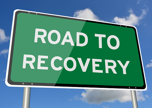 Road to recovery signpost against blue sky