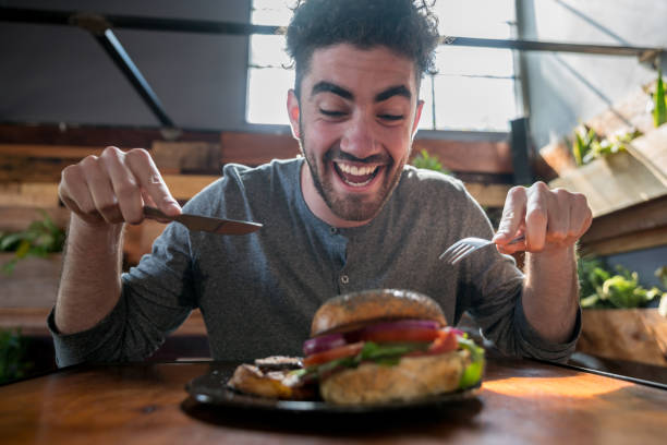 istock Very hungry young man diving into his burger using cutlery 915352696