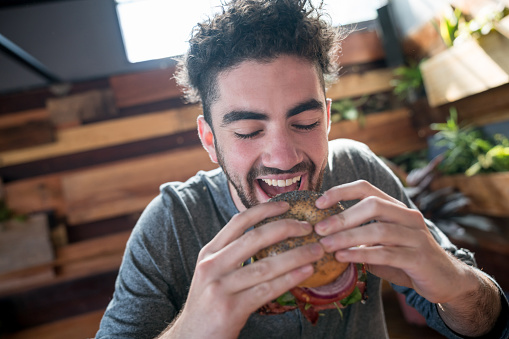 Satiesfied young man taking a bite of a burger with eyes closed looking very happy