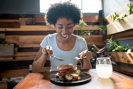 Beautiful african american woman eating a delicious bagel with vegetables at a restaurant looking happy and very hungry