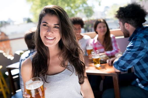 Pretty latin american woman enjoying a beer at a bar looking very happy and smiling