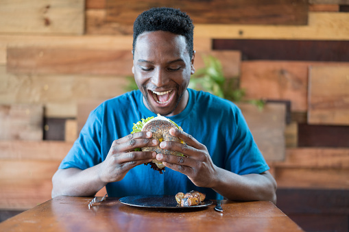 Happy black man holding a bagel with vegetables ready to eat it at a restaurant