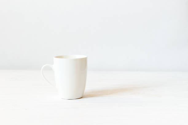 istock White cup mockup. Empty mug on wooden white background 915362632