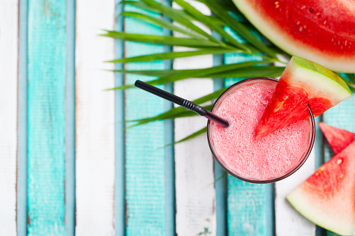 Watermelon smoothie, fresh juice on colorful wooden background with palm leaves. Top view. Copy space.