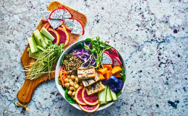 colorful buddha bowl with copy space composition, bowl has blood orange, grilled tofu, dragog fruit, sweet potato, pea shoots and chickpeas