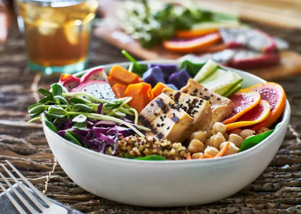 colorful buddha bowl with grilled tofu and pea shoots on table top