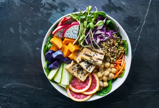 colorful buddha bowl with grilled tofu and dragon fruit shot from birds eye view on dark slate