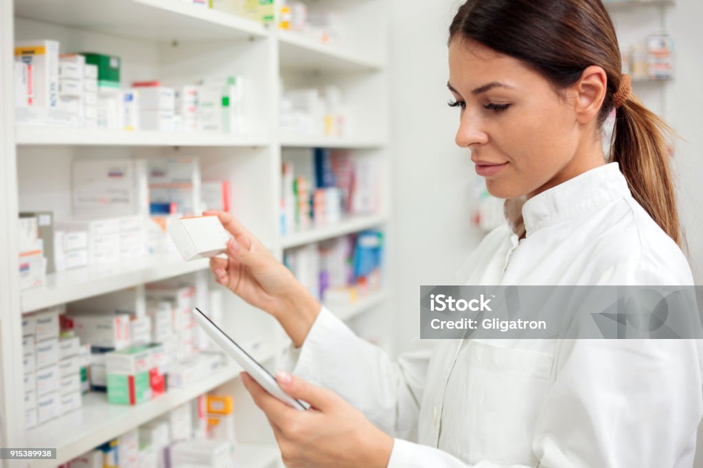 Serious young female pharmacist using tablet Medicine, pharmaceutics, health care and people concept - Serious young female pharmacist taking medications from the shelf. Pharmacist Stock Photo