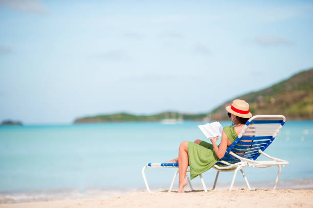 istock Young woman reading book on sunbed on sandy white beach 915399430