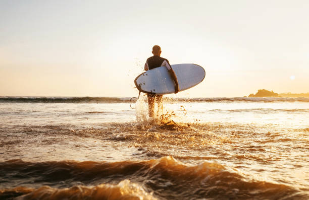 istock Surfer runs with surfboard towards ocean waves ta sunset time 915399750