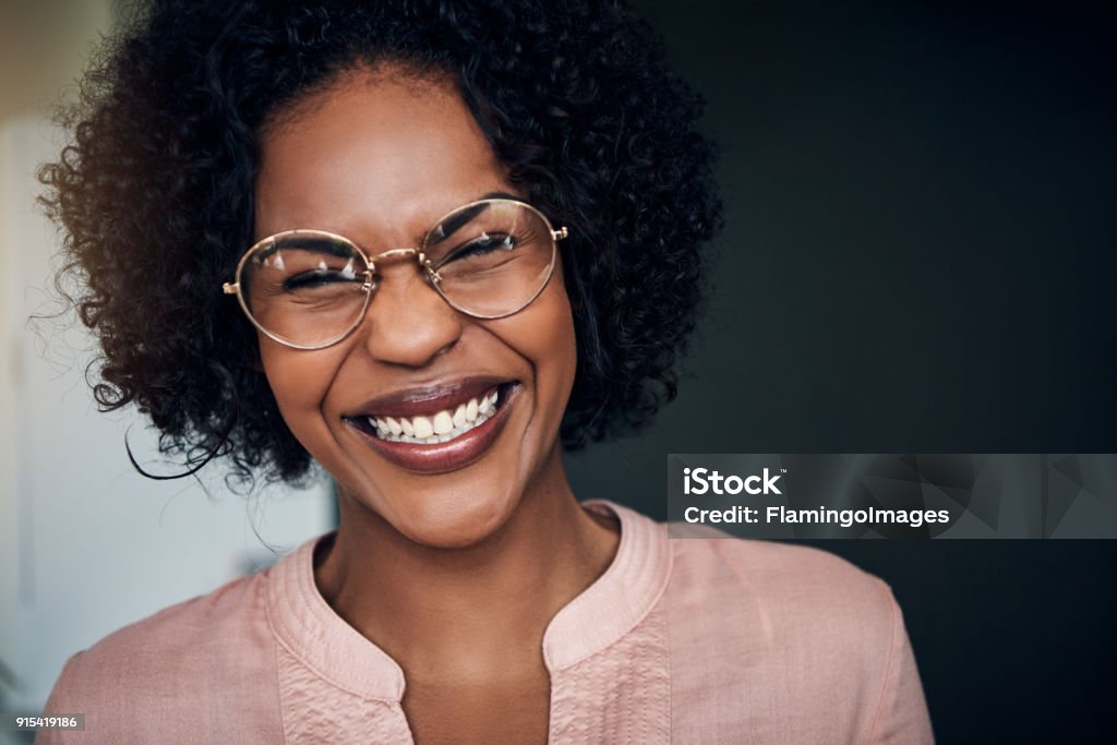 Laughing young African businesswoman standing alone in a modern office Young African businesswoman wearing glasses and lauging while standing alone in a modern office Laughing Stock Photo