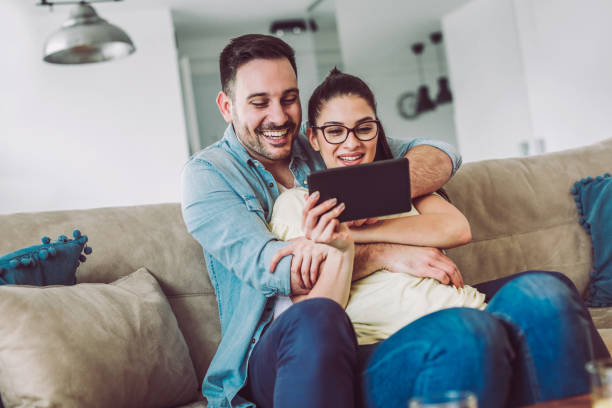 istock Tender smiling couple with digital tablet sitting on sofa at home 915426120