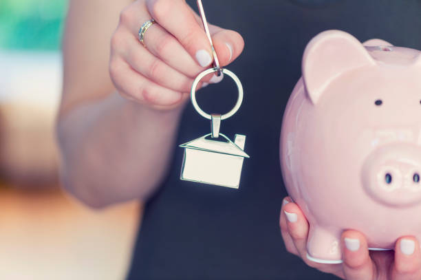 Woman holding house keys and a piggy bank. Woman holding house keys and a piggy bank. The key ring is house shaped. Close up. Home ownership and savings concept. Copy space. australia house home interior housing development stock pictures, royalty-free photos & images