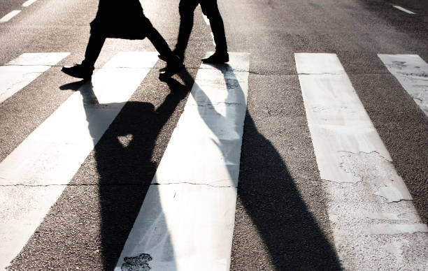 Pedestrians crossing the street City zebra crossing with two blurry walking pedestrians making long shadows in black and white high contrast crossing photos stock pictures, royalty-free photos & images