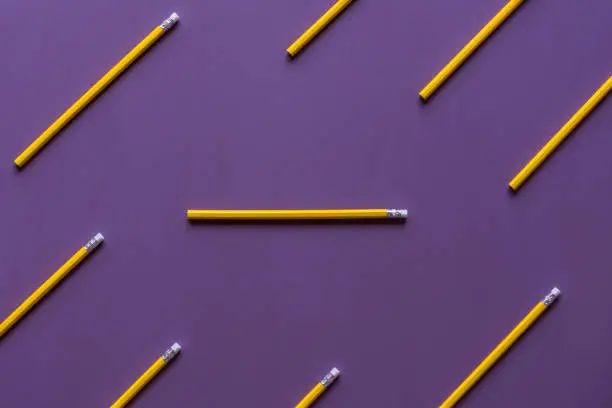 Wooden pencils with eraser tops arranged parallelly and only  one in horizontally, out of context, with space for text, on a purple background.
