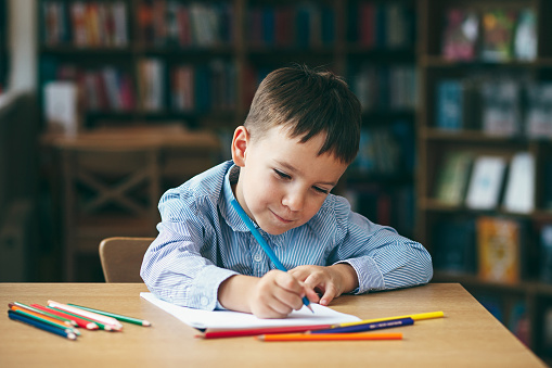 Cute  boy doing homework,  coloring pages, writing and painting. Children paint. Kids draw. Preschooler with books at home. Preschoolers learn to write and read. Creative boy.