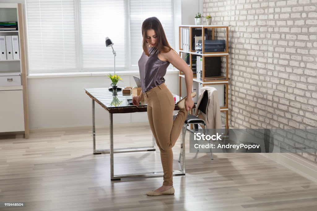 Businesswoman Stretching Her Leg In Office Young Businesswoman Stretching Her Leg At Workplace In Office Exercising Stock Photo