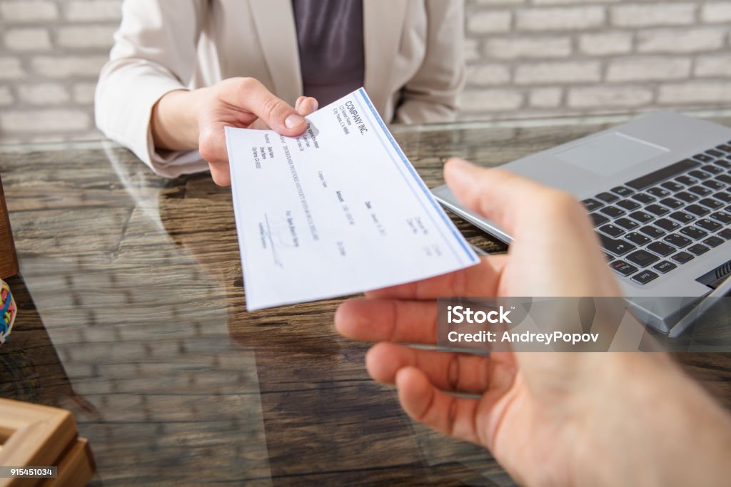 Businesswoman Giving Cheque To Her Colleague Close-up Of A Business Woman Giving Cheque To Her Colleague At Workplace In Office Check - Financial Item Stock Photo