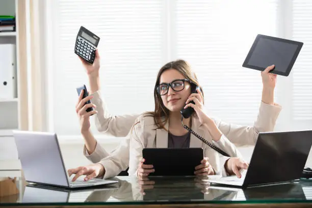 Busy Young Smiling Businesswoman With Six Arms Doing Different Type Of Work In Office