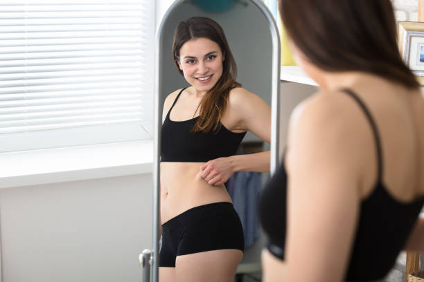 reflexión de mujer pinches grasa en su vientre - dieting mirror healthy lifestyle women fotografías e imágenes de stock