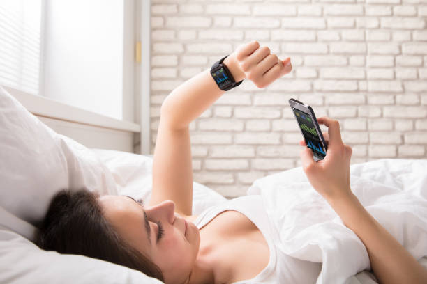 femme sur lit synchronisation intelligente watch avec téléphone portable - traqueur de gibier photos et images de collection