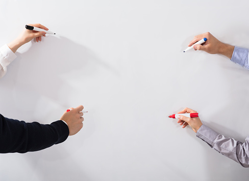 Close-up Of Business People's Hands Holding Different Marker Writing On Whiteboard