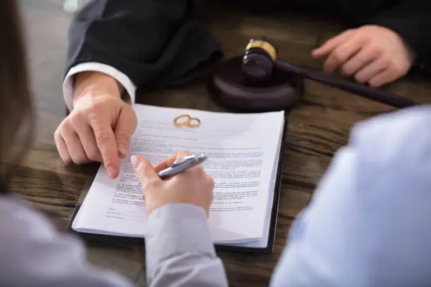 Close-up Of A Female Signing Contract On Desk In Courtroom