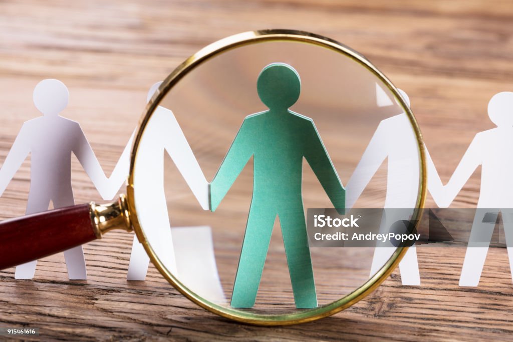 Magnifying Glass On Cut-out Figures Magnifying Glass On Cut-out Figures On Wooden Desk Recruitment Stock Photo