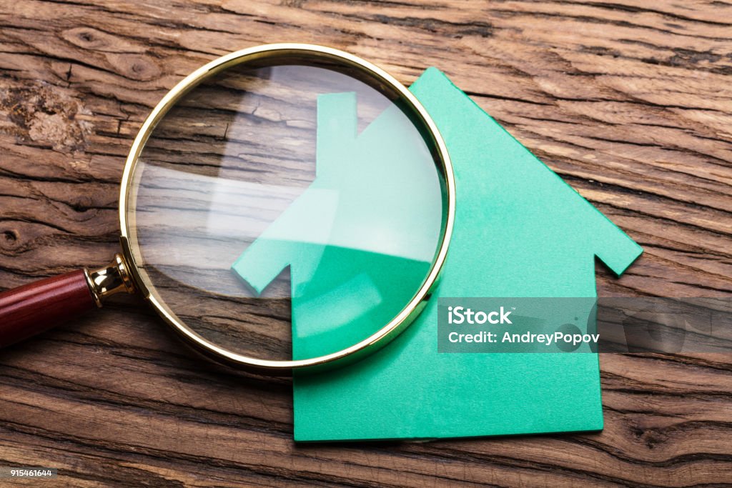 Magnifying Glass And Green Paper House Closeup Of Magnifying Glass And Green Paper House On Wood Examining Stock Photo