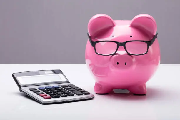 Close-up Of A Piggybank With Eyeglasses And Calculator On Desk