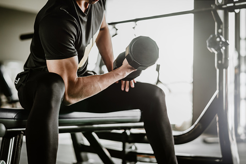 cropped shot of fitness man doing concentration curls exercise working out with dumbbell in gym. Weight training concept.