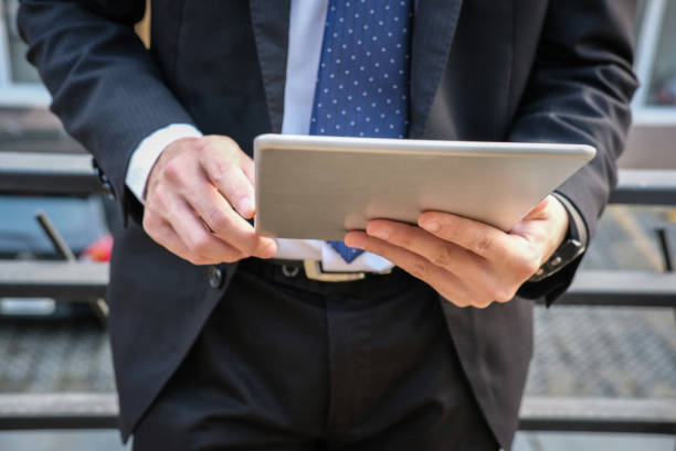istock businessman in suit holding touchpad while standing outside building. young asian man using digital tablet for work outdoors 915483284