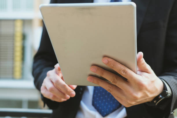 istock businessman in suit holding touchpad while standing outside building. young asian man using digital tablet for work outdoors 915483288